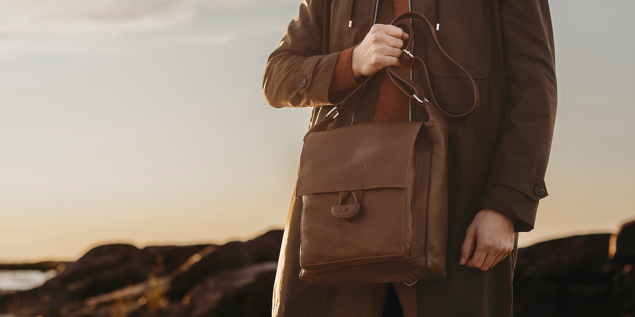 Ruskeatakkinen mies pitelee kädessään rouheaa miestenlaukkua.